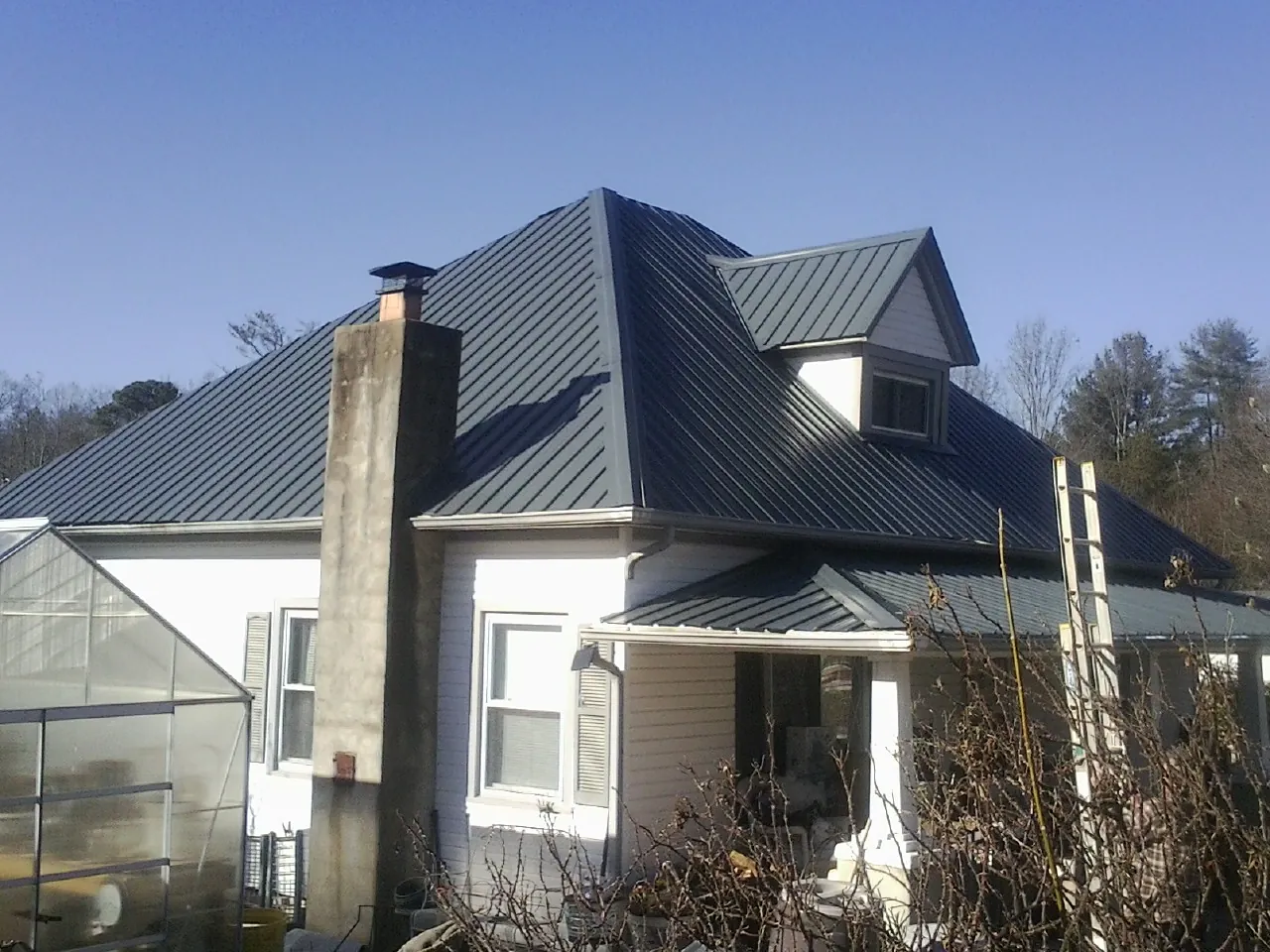 Dark blue standing seam metal roof on a white farmhouse with dormer — Slate & Tile Roof Repair by Roofing Brothers in Paxtonville