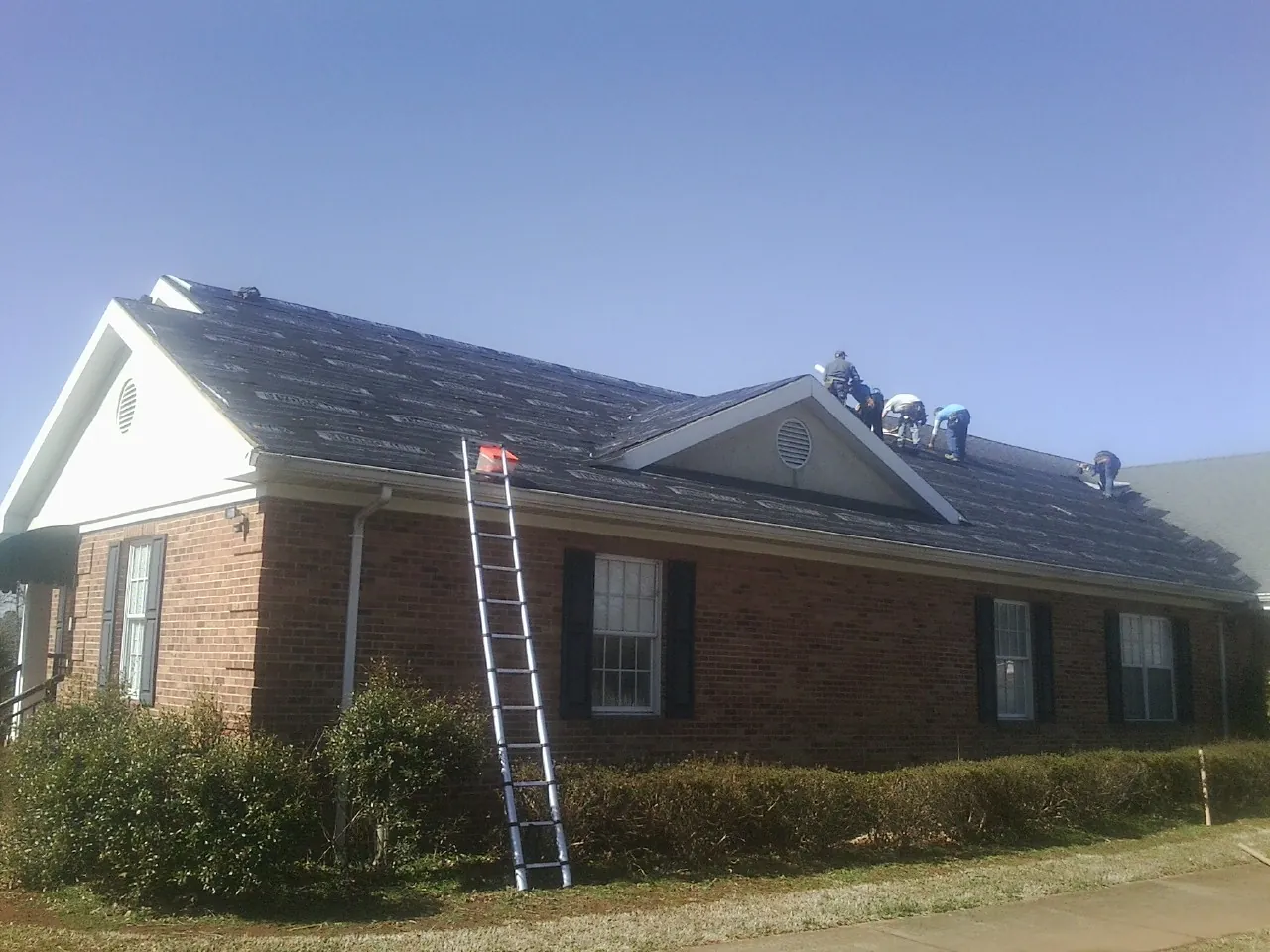 Crew tearing shingles off a brick ranch roof with a ladder set — Metal Roof Repair work by our crew in Paxtonville