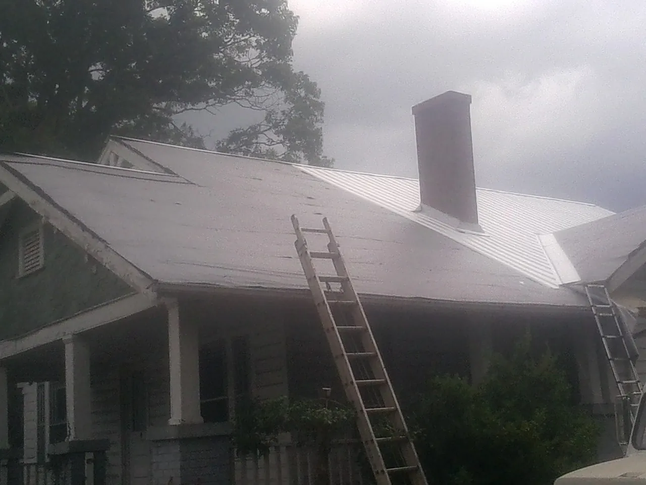 Ladders against a metal roof on an older home with a brick chimney in Paxtonville