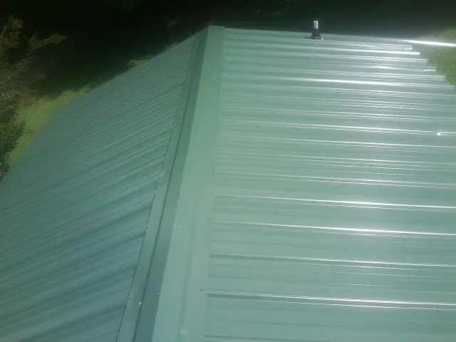 New green metal panels meeting at the ridge of a roof — Flat Roof Repair work by our crew in Paxtonville