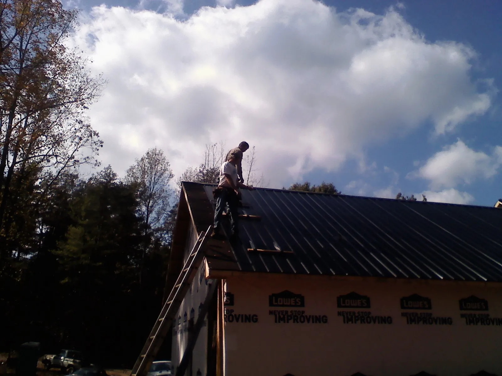 Roofer fastening dark metal panels high against a cloudy sky, from a Roof Inspection job in Paxtonville