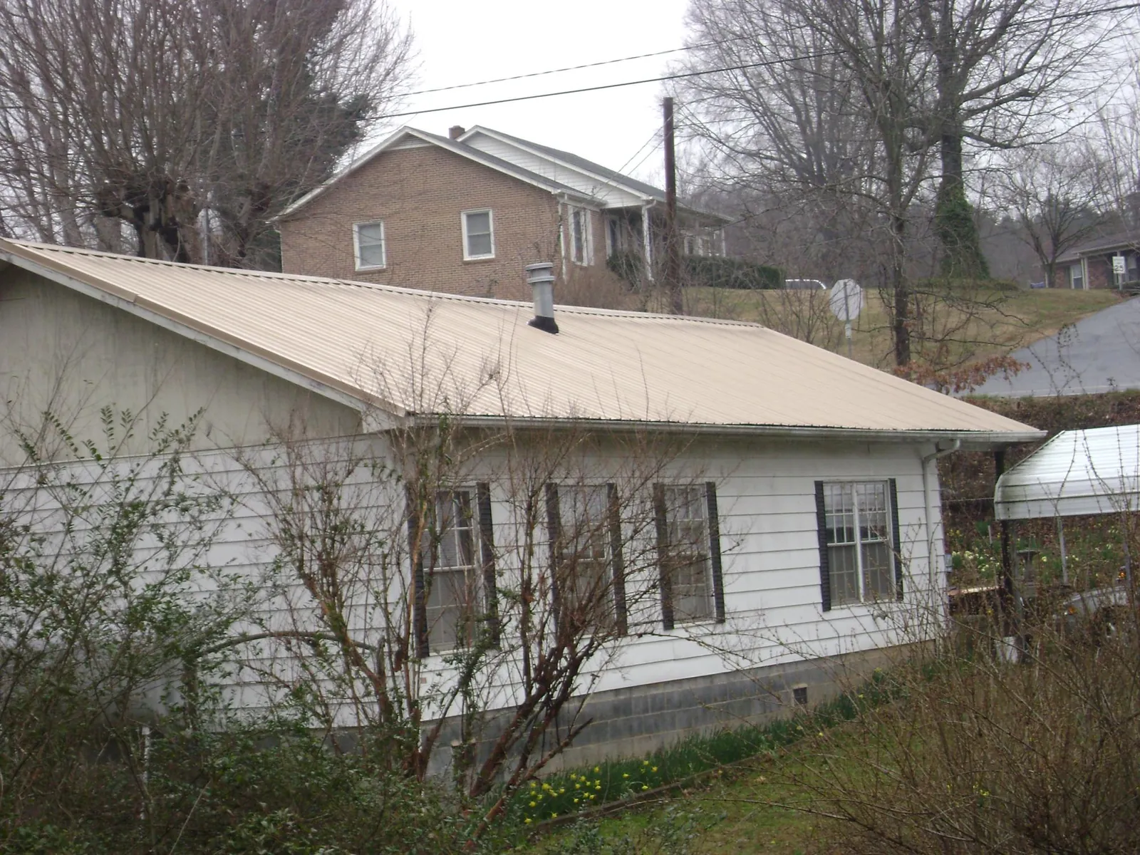 Tan metal roof on a white sided house set into a hillside — Commercial Roofing by Roofing Brothers in Paxtonville